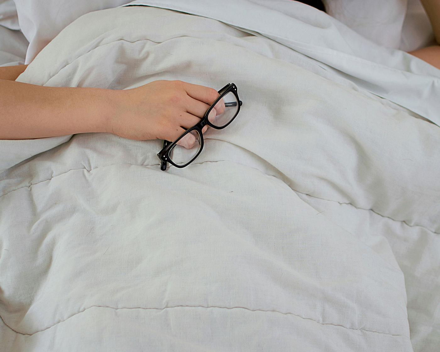 Schwarze Brille auf weiß bezogenem Bett